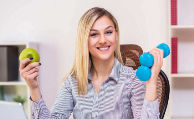 beautiful businesswoman holding apple and weights while working in her office