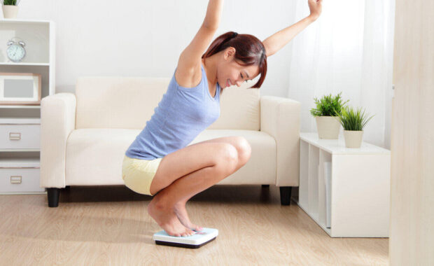 woman smiling on weighing scales at home