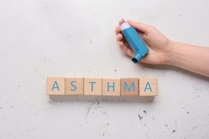 asthma made of wooden cubes and female hand with inhaler on light background