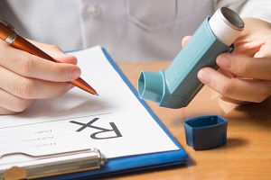 doctor hand holding blue asthma inhaler and writing medical prescription