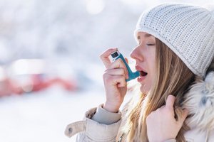 A woman is using an inhaler to breathe in cold weather