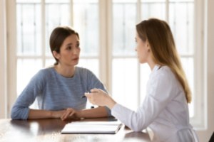 A female doctor is collecting data on medical history from a woman and taking notes