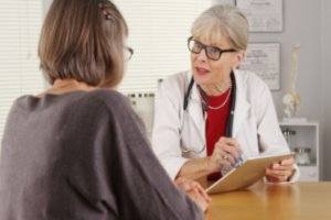 A senior doctor is asking and noting health details from a woman in her clinic
