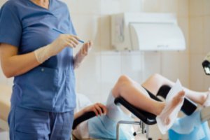 An unrecognized female doctor is taking a sample for the pap smear test while the patient is lying on the bed