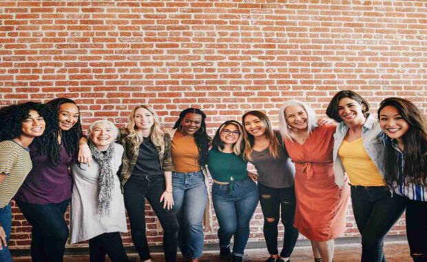 Ten women of different age groups standing together and smiling