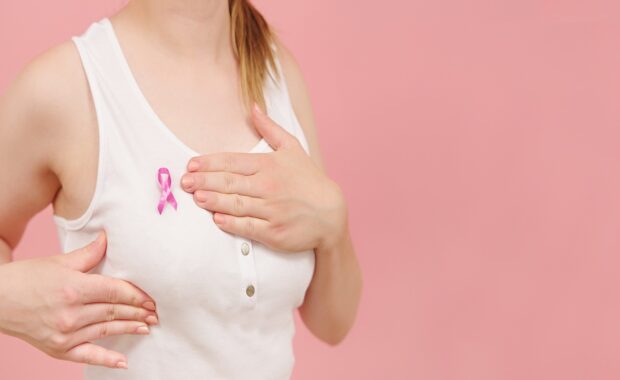 A woman wearing a cancer ribbon checking her breasts