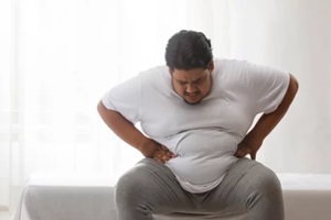 an obese man sitting and holding his belly in pain
