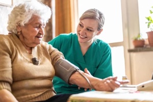 female caretaker measuring senior woman's blood pressure at home