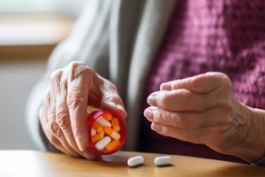 close up of old woman closes pill bottle to take cholesterol medicine