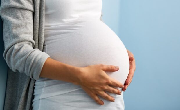 Durham, NC woman during last months of pregnancy holding her big belly gently standing against wall in blue room