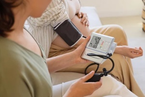 young pregnant woman with doula measuring blood pressure on sofa at home, closeup