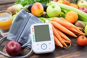 Blood pressure monitor and fresh fruits with vegetables against wooden table