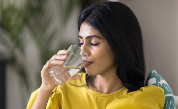 peaceful satisfied young Indian woman drinking fresh pure water with closed eyes at home