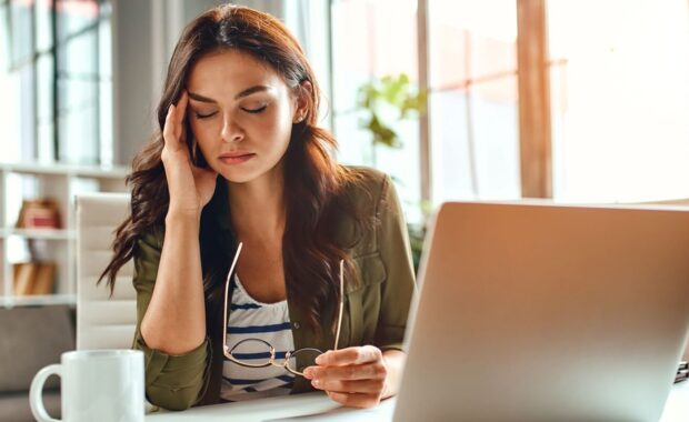 business woman in stress works at a laptop while sitting at a table at home and holds her hand on her temples, migraine attack