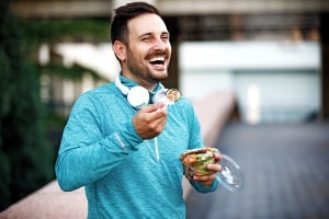 Happy Man with Headphones Eating Vegetable Salad