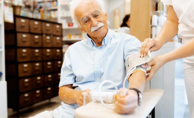 female pharmacist checking an elderly man blood pressure in a pharmacy