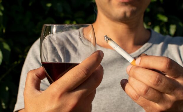 man holding cigarette and glass with wine