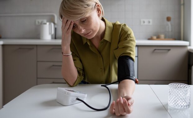 middle aged woman with fatigue and headache feeling sick and measures blood pressure level with tonometer