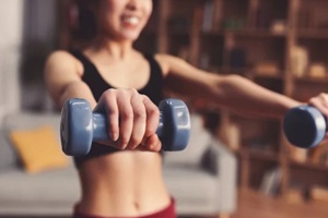 woman holds dumbbells out in front of her as she exercises in her living room