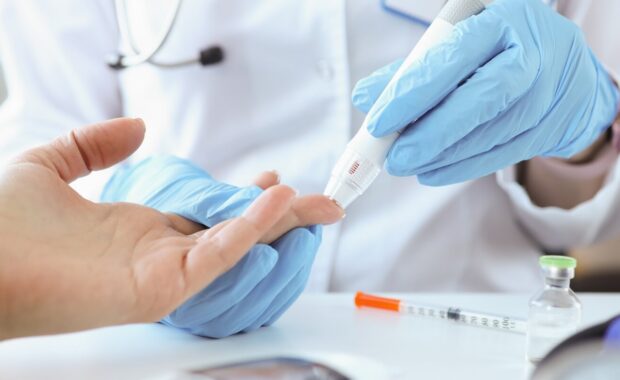 doctor with gloves piercing patients finger with lancet closeup