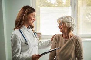 happy female nurse talking to her senior patient at doctor's office