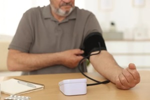 man measuring blood pressure with sphygmomanometer at table indoors, closeup